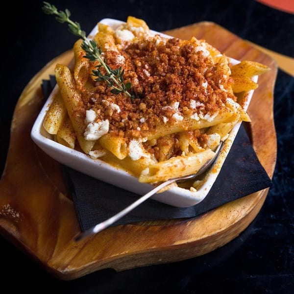 Creamy mac and cheese with breadcrumbs and a sprig of thyme in a white dish.