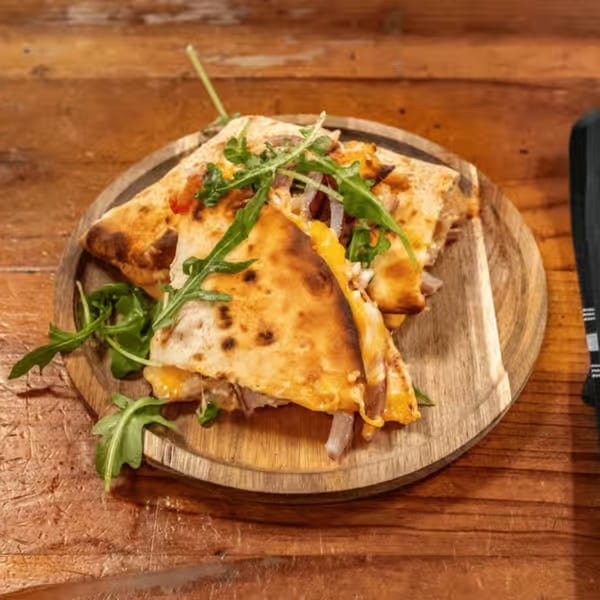 Quesadilla slices with melted cheese, meat, and arugula on a wooden board.