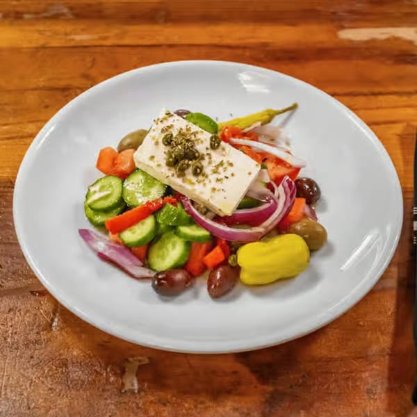 A vibrant Greek salad with a large block of feta cheese, olives, cucumbers, tomatoes, and red onions.
