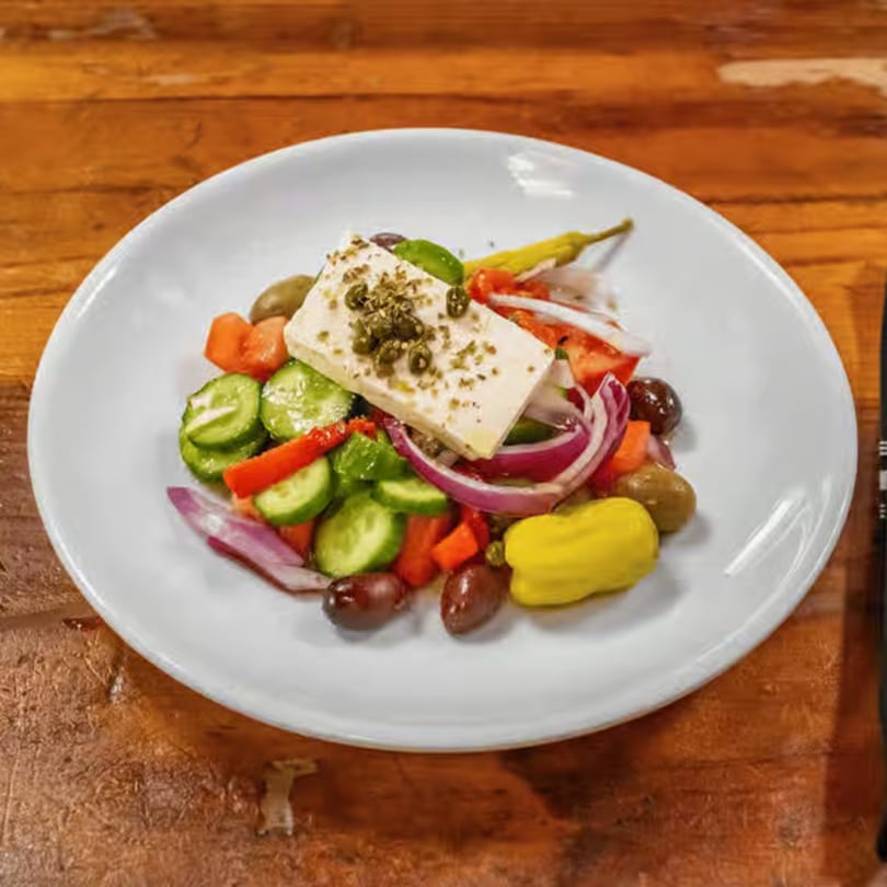 A vibrant Greek salad with a large block of feta cheese, olives, cucumbers, tomatoes, and red onions.