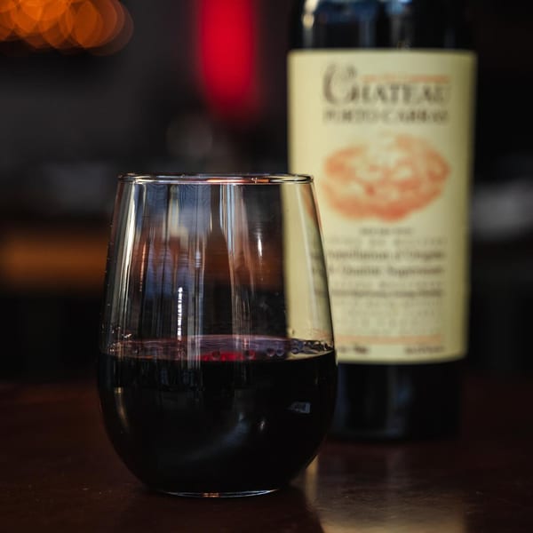 A stemless glass of red wine sits next to a bottle of Chateau wine on a dark table.